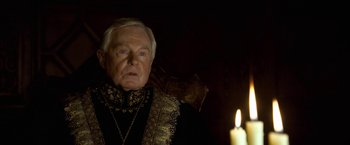 Movie still from “The Golden Compass” (2007), directed by Chris Weitz – An older man in a black and gold outfit with a candle in the background; Close Up shot, Over the shoulder angle
