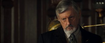 Movie still from “The Golden Compass” (2007), directed by Chris Weitz – An older man in a suit and tie looking sad; Close Up shot, Over the shoulder angle