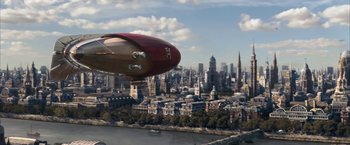 Movie still from “The Golden Compass” (2007), directed by Chris Weitz – An airplane flying over a large city with buildings in the background; Extreme Wide shot, Low angle
