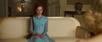 Movie still from “The Golden Compass” (2007), directed by Chris Weitz – A girl in a blue dress sitting on a white couch; Medium shot, High angle