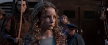 Movie still from “The Golden Compass” (2007), directed by Chris Weitz – A young girl with curly hair is standing in front of two other people; Close Up shot, Low angle