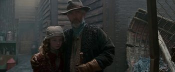 Movie still from “The Golden Compass” (2007), directed by Chris Weitz – An older man and a young girl standing next to each other in front of a building; Medium shot, Over the shoulder angle