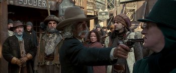 Movie still from “The Golden Compass” (2007), directed by Chris Weitz – An old man wearing a cowboy hat is holding a gun; Medium shot, Over the shoulder angle