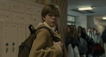 Movie still from “The Goldfinch” (2019), directed by John Crowley – A young boy wearing glasses and holding a backpack; Medium shot, Low angle