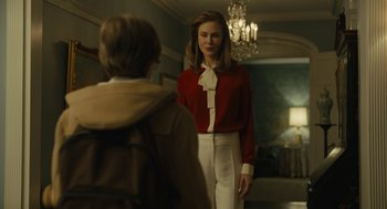 Movie still from “The Goldfinch” (2019), directed by John Crowley – A woman in a red and white outfit standing in front of a man; Medium shot, Over the shoulder angle