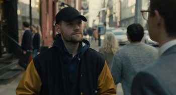 Movie still from “The Goldfinch” (2019), directed by John Crowley – A man with a beard wearing a black and yellow jacket and a black hat; Close Up shot, Over the shoulder angle