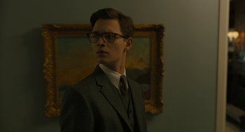 Movie still from “The Goldfinch” (2019), directed by John Crowley – A man in a suit and tie standing in front of a painting; Medium shot, Low angle