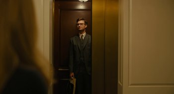 Movie still from “The Goldfinch” (2019), directed by John Crowley – A man in a suit standing in an elevator; Medium shot, Low angle