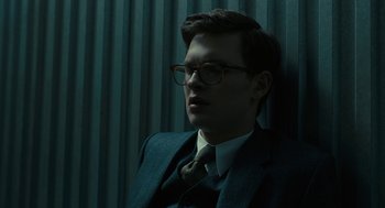 Movie still from “The Goldfinch” (2019), directed by John Crowley – A man in a suit and tie sitting in front of a curtain; Close Up shot, Low angle
