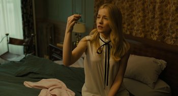 Movie still from “The Goldfinch” (2019), directed by John Crowley – A woman sitting on a bed holding a piece of paper; Medium shot, High angle