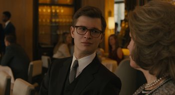Movie still from “The Goldfinch” (2019), directed by John Crowley – A man in a suit and tie in front of a group of people; Close Up shot, Over the shoulder angle