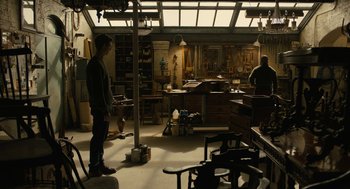 Movie still from “The Goldfinch” (2019), directed by John Crowley – A man standing in front of a table in a room; Wide shot, High angle