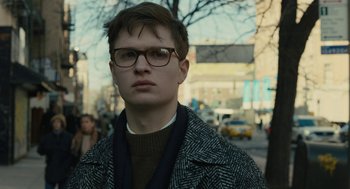 Movie still from “The Goldfinch” (2019), directed by John Crowley – A young man wearing glasses standing on the sidewalk; Close Up shot, Over the shoulder angle