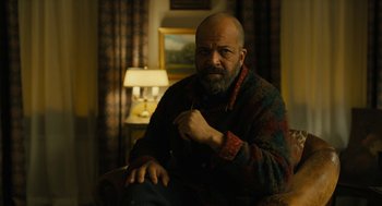Movie still from “The Goldfinch” (2019), directed by John Crowley – A man sitting in a chair in front of a lamp; Medium shot, Low angle