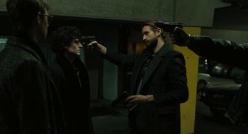 Movie still from “The Goldfinch” (2019), directed by John Crowley – Two men in black jackets holding guns in a room; Medium shot, Over the shoulder angle