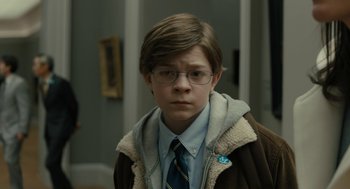 Movie still from “The Goldfinch” (2019), directed by John Crowley – A young boy wearing glasses and a jacket; Close Up shot, Over the shoulder angle