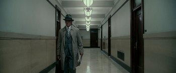 Movie still from “The Good Shepherd” (2006), directed by Robert De Niro – A man in a hat and a coat walking down a hallway; Wide shot, Low angle