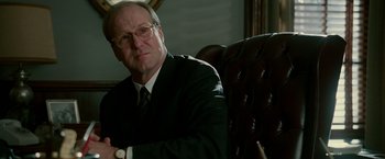 Movie still from “The Good Shepherd” (2006), directed by Robert De Niro – A man in a suit and tie sitting in a chair; Close Up shot, Over the shoulder angle