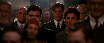 Movie still from “The Good Shepherd” (2006), directed by Robert De Niro – A man in a suit and tie standing in front of a group of people; Close Up shot, Over the shoulder angle
