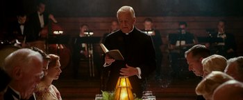 Movie still from “The Good Shepherd” (2006), directed by Robert De Niro – A priest reading a book in front of a group of people; Medium shot, Low angle