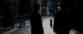Movie still from “The Good Shepherd” (2006), directed by Robert De Niro – A man wearing a hat standing in the dark; Wide shot, Over the shoulder angle