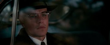 Movie still from “The Good Shepherd” (2006), directed by Robert De Niro – A person wearing glasses and a hat; Close Up shot, Over the shoulder angle