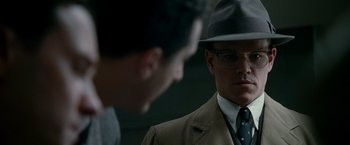 Movie still from “The Good Shepherd” (2006), directed by Robert De Niro – A man in a hat and glasses is looking at another man in a suit; Close Up shot, Over the shoulder angle