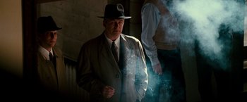 Movie still from “The Good Shepherd” (2006), directed by Robert De Niro – A man wearing a hat and a suit and smoking a cigarette; Medium shot, Low angle