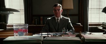 Movie still from “The Good Shepherd” (2006), directed by Robert De Niro – A man sitting at a desk in front of papers; Medium shot, Over the shoulder angle