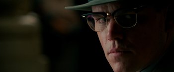 Movie still from “The Good Shepherd” (2006), directed by Robert De Niro – A person wearing glasses and a hat; Close Up shot, Over the shoulder angle