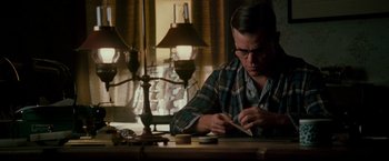 Movie still from “The Good Shepherd” (2006), directed by Robert De Niro – A man sitting at a table writing on a piece of paper; Medium shot, Low angle