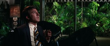 Movie still from “The Graduate” (1967), directed by Mike Nichols – A man in a suit holding a glass of wine; Medium shot, Low angle