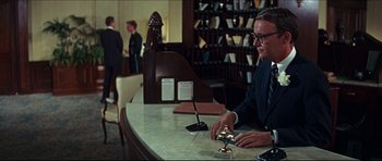 Movie still from “The Graduate” (1967), directed by Mike Nichols – A man sitting at a counter in front of a bell; Medium shot, Low angle