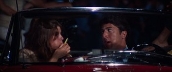 Movie still from “The Graduate” (1967), directed by Mike Nichols – A man and a woman in a red car eating a banana; Close Up shot, Over the shoulder angle