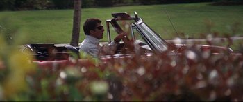 Movie still from “The Graduate” (1967), directed by Mike Nichols – A man driving a red car through a lush green park; Wide shot, Low angle