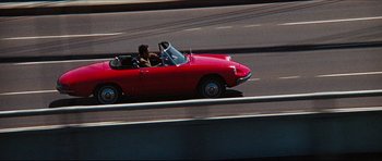 Movie still from “The Graduate” (1967), directed by Mike Nichols – A man driving a red car down a street; Wide shot, High angle