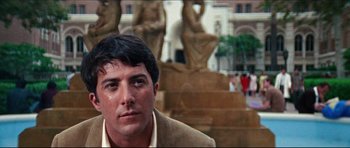 Movie still from “The Graduate” (1967), directed by Mike Nichols – A person wearing a suit near statues; Close Up shot, Low angle