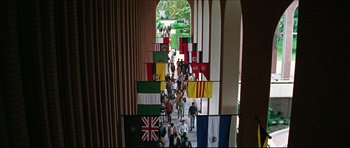 Movie still from “The Graduate” (1967), directed by Mike Nichols – A crowd of people walking down a walkway with flags; Extreme Wide shot, High angle