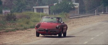Movie still from “The Graduate” (1967), directed by Mike Nichols – A man driving a red car down a dirt road; Wide shot, High angle