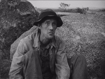 Movie still from “The Grapes of Wrath” (1940), directed by John Ford – A man sitting on top of a pile of rocks; Close Up shot, Low angle