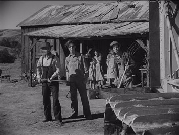Movie still from “The Grapes of Wrath” (1940), directed by John Ford – A black and white photo of a group of men standing in front of a building; Wide shot, Low angle
