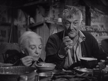Movie still from “The Grapes of Wrath” (1940), directed by John Ford – An older man and a woman sitting at a dinner table; Medium shot, Low angle