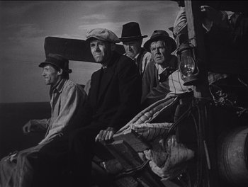 Movie still from “The Grapes of Wrath” (1940), directed by John Ford – A black and white photo of a group of men sitting on a bench; Medium shot, Low angle