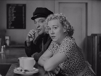 Movie still from “The Grapes of Wrath” (1940), directed by John Ford – An older man and woman sitting at a table with a cup of coffee; Medium shot, High angle