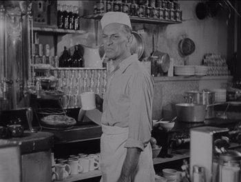 Movie still from “The Grapes of Wrath” (1940), directed by John Ford – A man standing in a kitchen holding a cup; Medium shot, Low angle