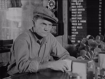 Movie still from “The Grapes of Wrath” (1940), directed by John Ford – A man sitting at a table in front of a menu board; Close Up shot, Over the shoulder angle
