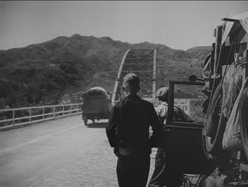 Movie still from “The Grapes of Wrath” (1940), directed by John Ford – A man standing next to a truck on a bridge; Wide shot, Low angle