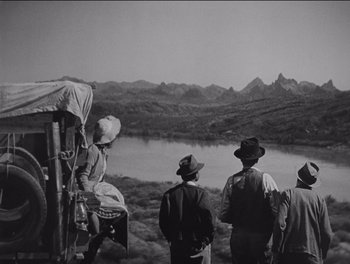 Movie still from “The Grapes of Wrath” (1940), directed by John Ford – A black and white photo of a group of men standing next to a body of water; Extreme Wide shot, High angle