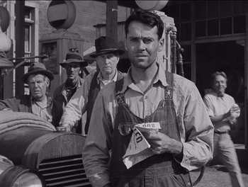 Movie still from “The Grapes of Wrath” (1940), directed by John Ford – An old photo of a man holding a license plate in front of other men; Medium shot, Low angle
