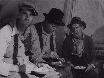 Movie still from “The Grapes of Wrath” (1940), directed by John Ford – A group of men sitting around a table eating; Medium shot, High angle